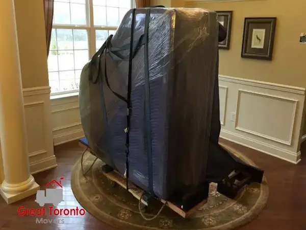 A piano in a living room, packed, and ready for transport by movers in Toronto.