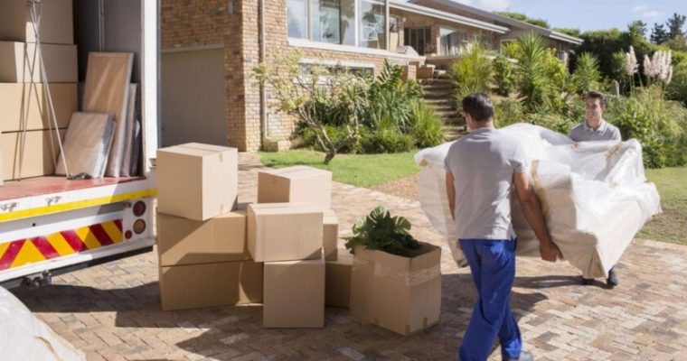 Two professional movers carrying a couch into a new home after a long distance relocation.